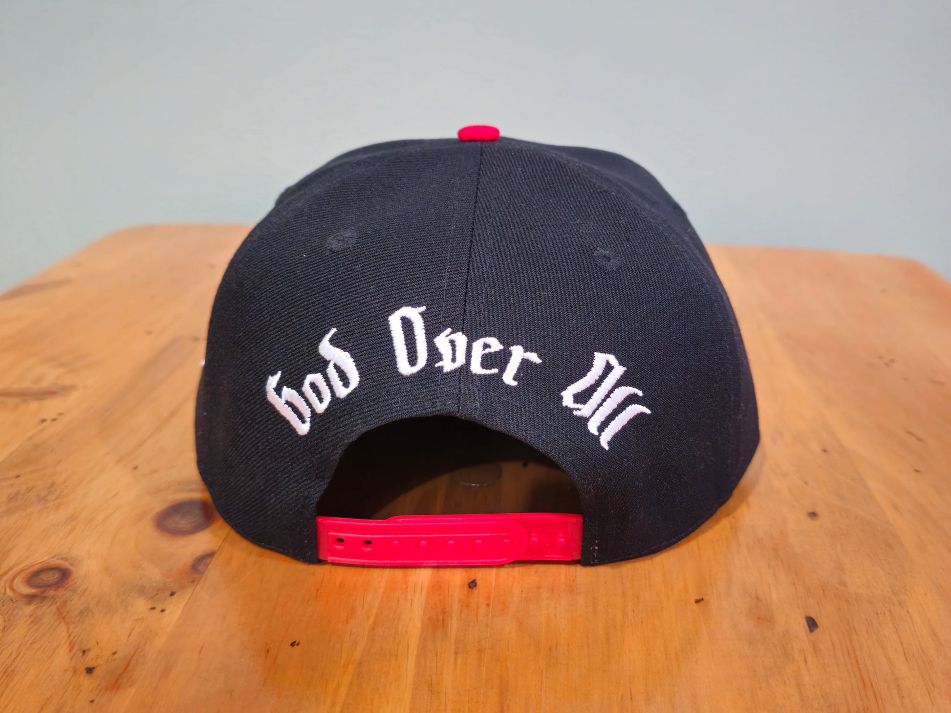 Black cap with 'God Over All' text on a wooden surface