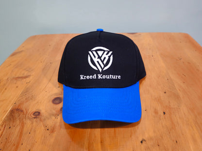 Black and blue cap with 'Kreed Kouture' logo on a wooden surface