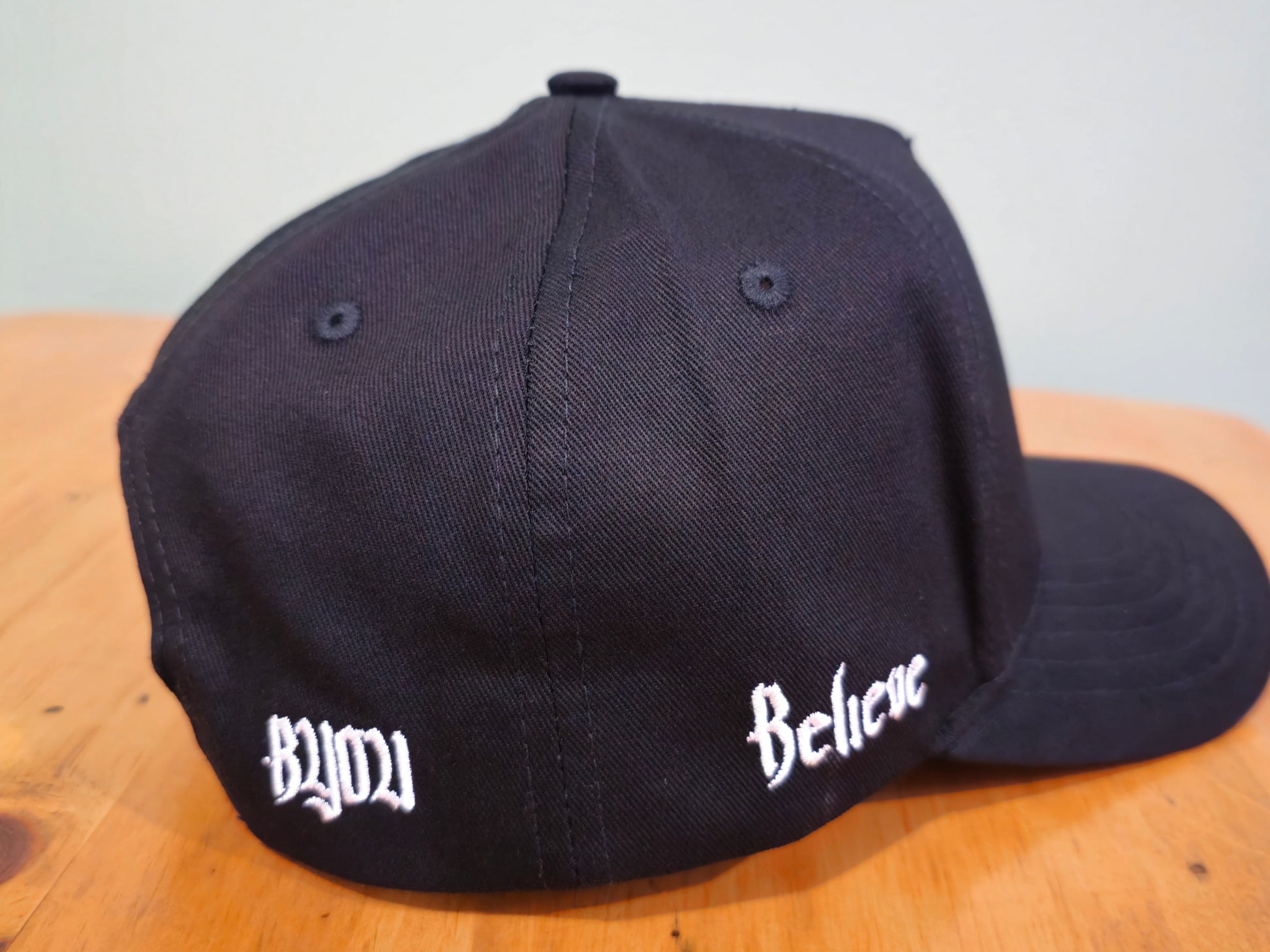 Black cap with 'Dyuu' and 'Believe' text on a wooden surface