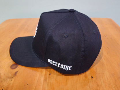 Black cap with 'overcome' text on a wooden surface