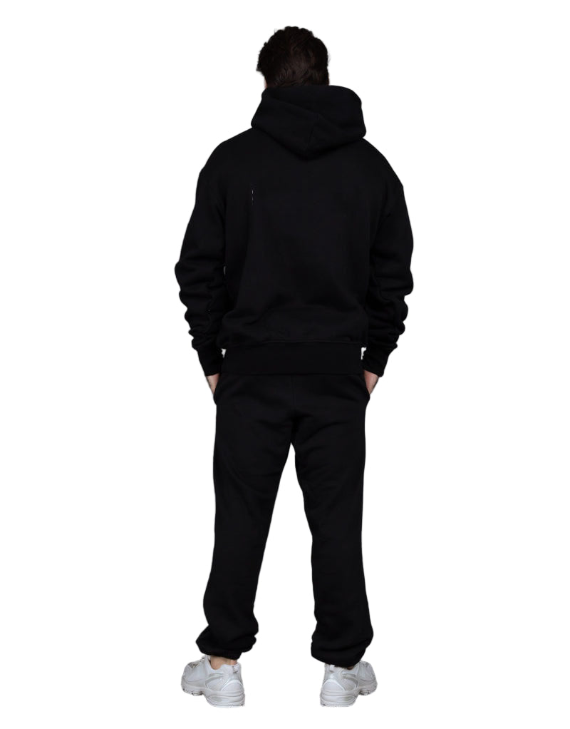 Person wearing a black hoodie and pants with white sneakers on a gray background