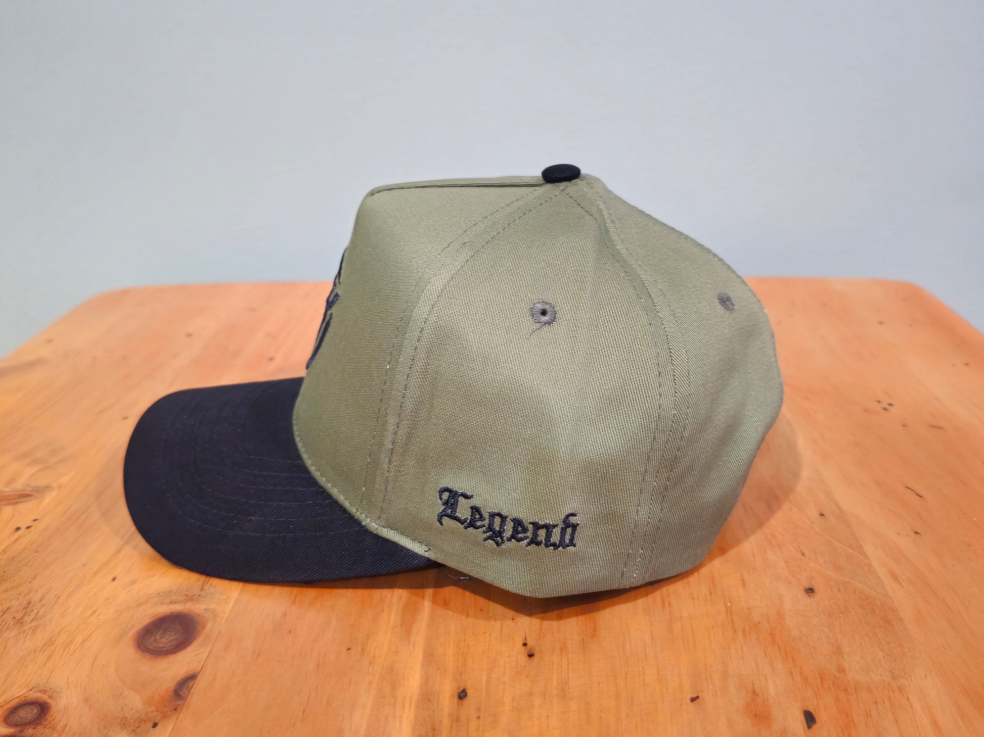 Two baseball caps, one green and one black, on a wooden surface with a light gray background.