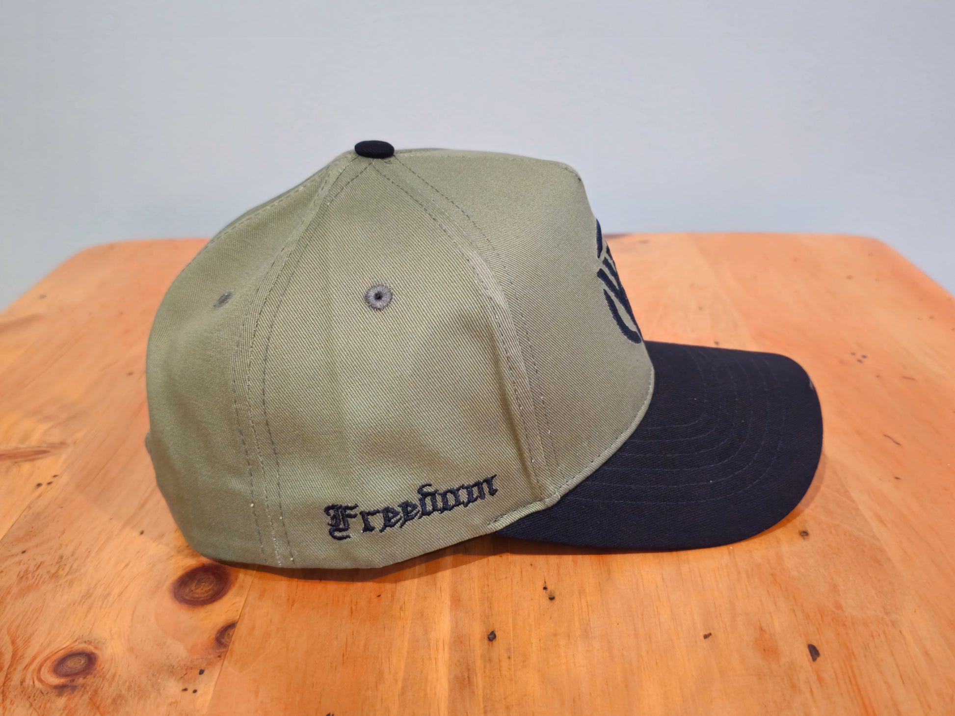 Two baseball caps, one beige and one black, on a wooden surface with a light gray background.