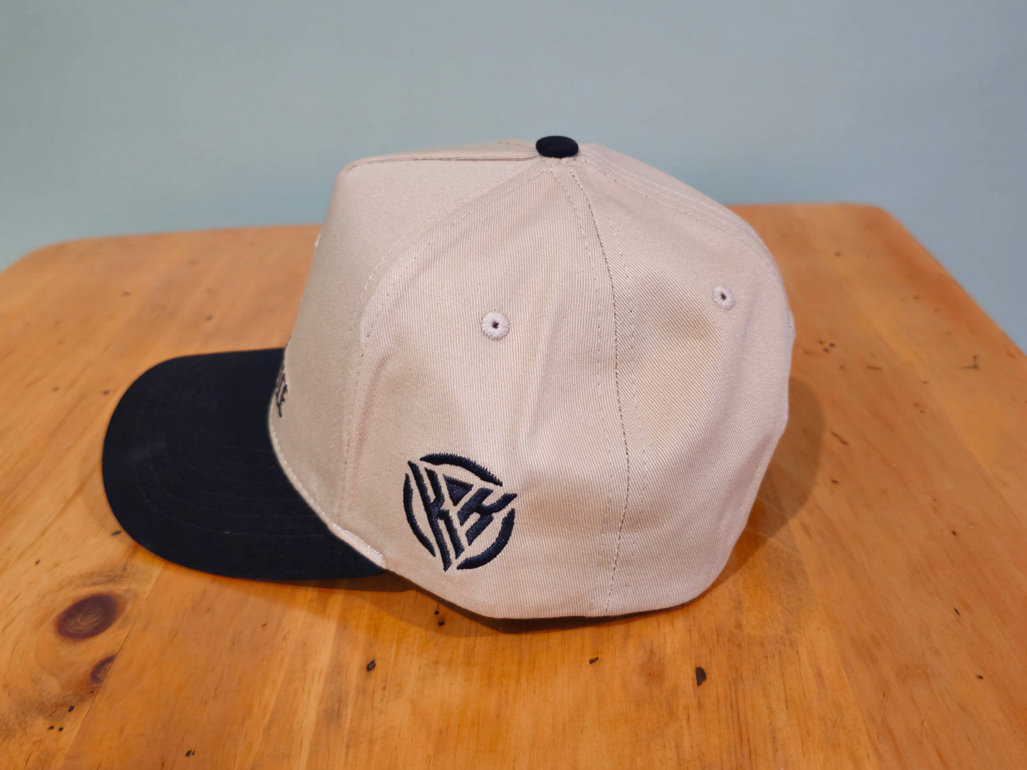 Beige and black baseball cap on a wooden surface with a light blue background