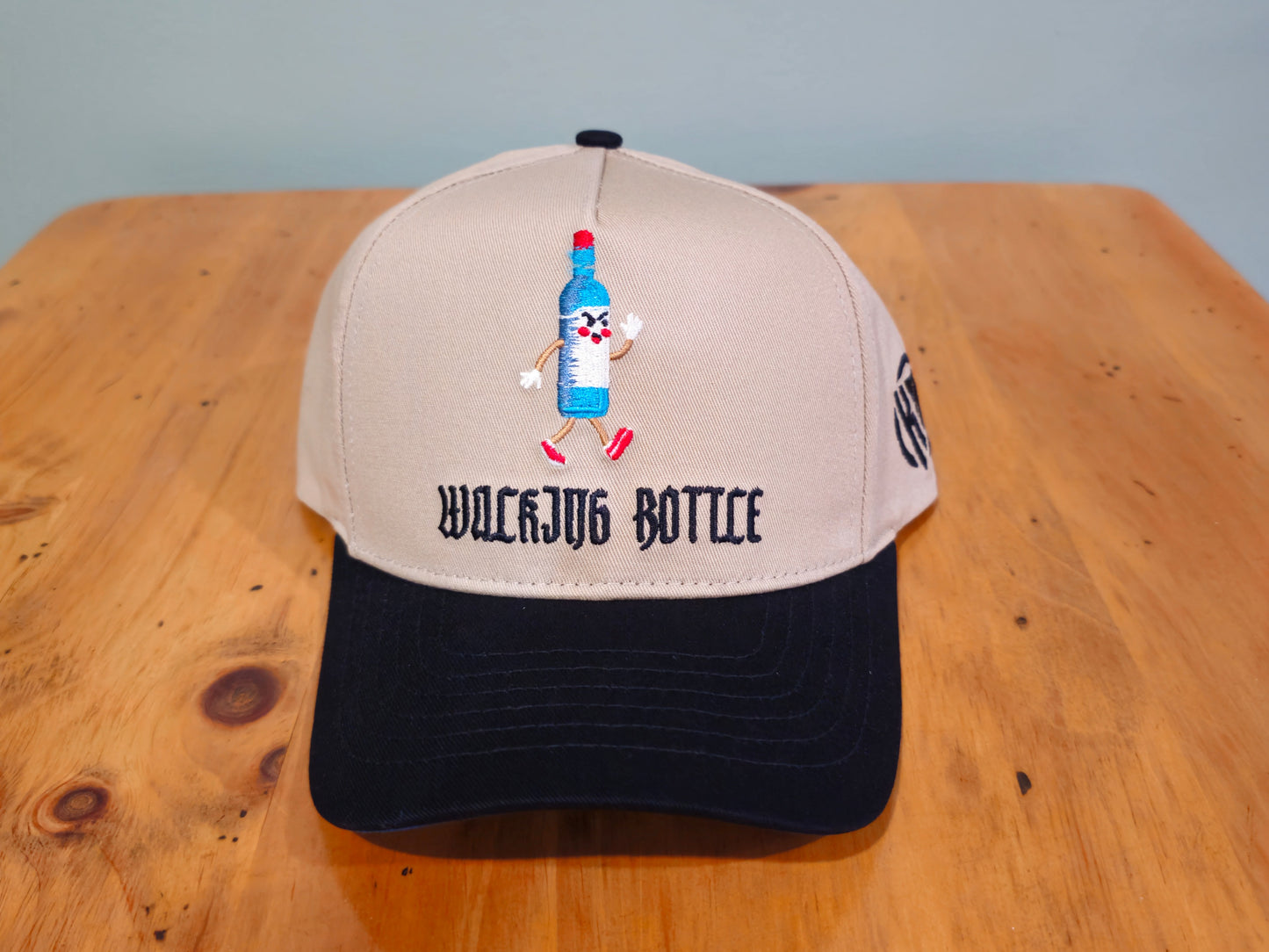 Beige and navy cap with cartoon bottle design on a wooden surface