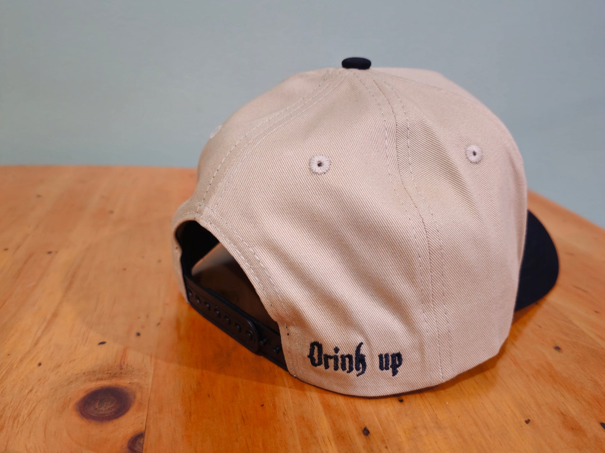 Beige cap with 'Drink up' text on a wooden surface