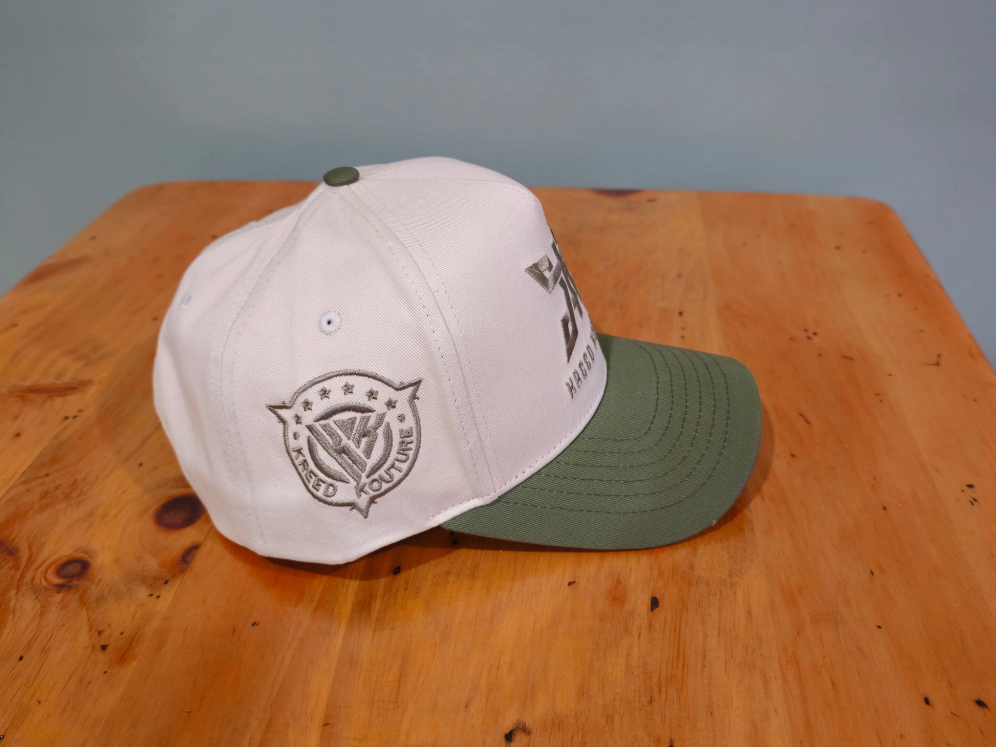 Two baseball caps, one white and one green, on a wooden surface with a gray background.