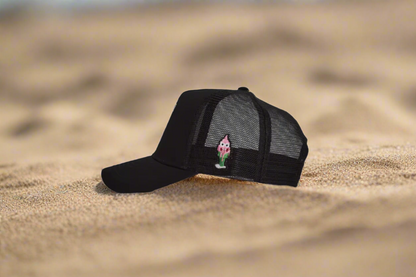 Black cap with a small embroidered design on a sandy surface
