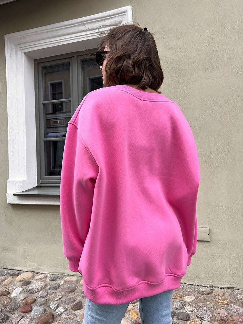 Person wearing a pink sweatshirt standing outside a building with a window.